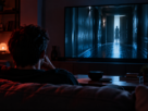 Pessoa assiste, em uma sala escura, a uma cena misteriosa exibida na televisão